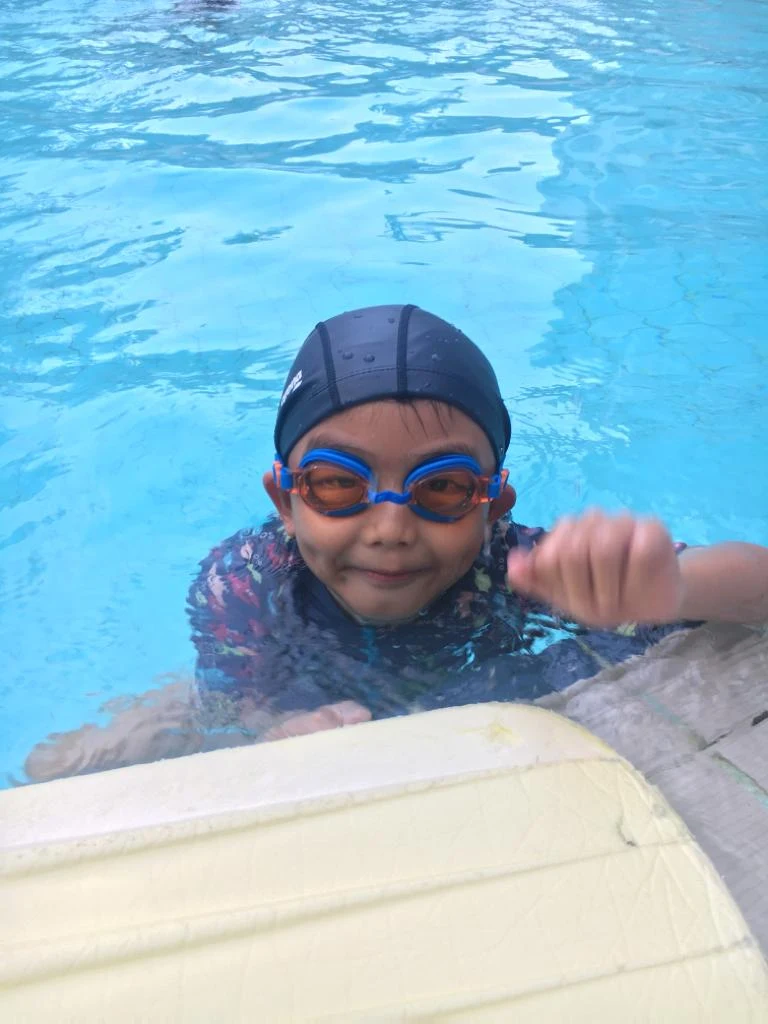 Young swimmer with goggles giving a thumbs up at the pool